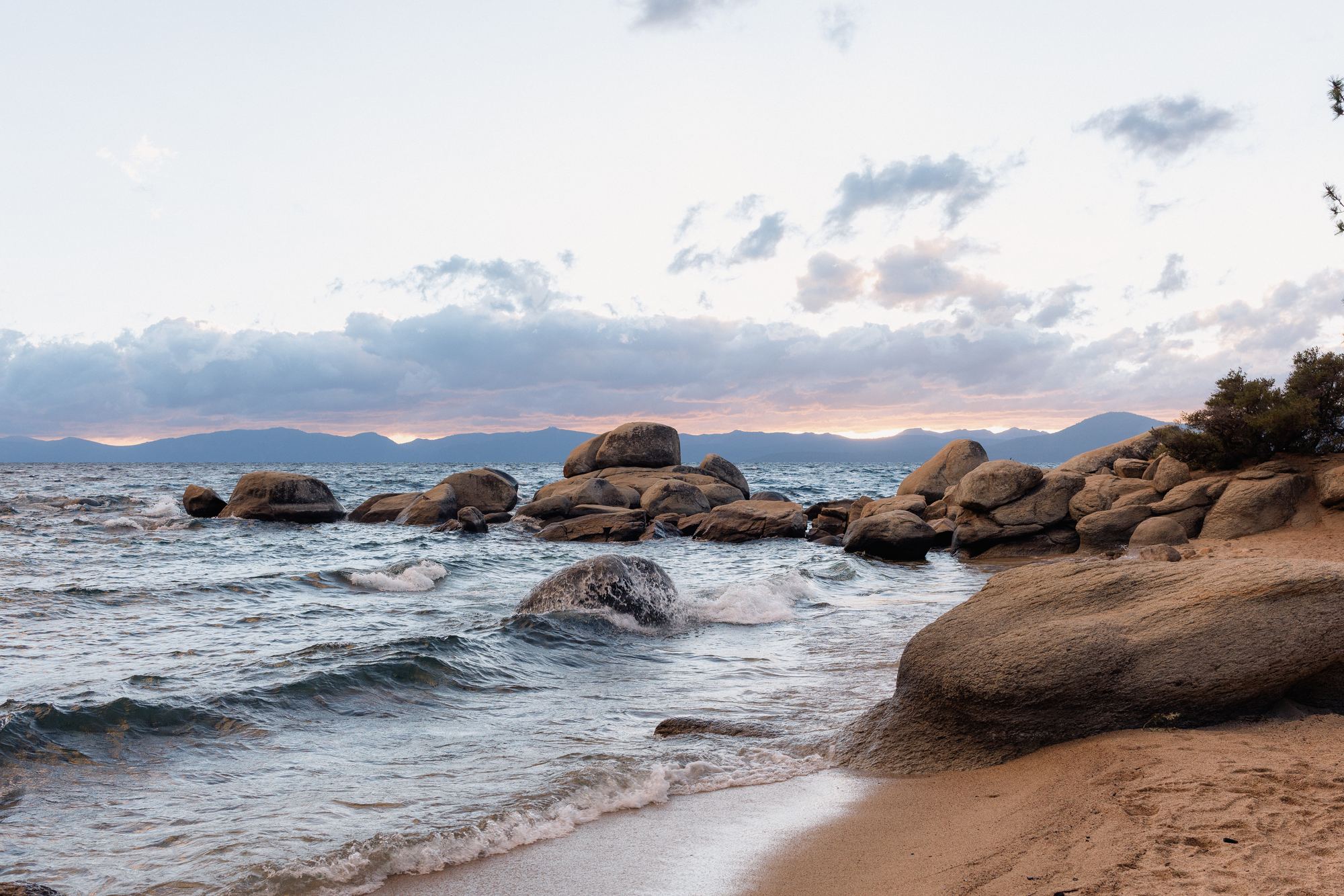 Granite boulders in the surf at dusk on Lake Tahoe's East Shore, the far shore's mountains on the horizon.