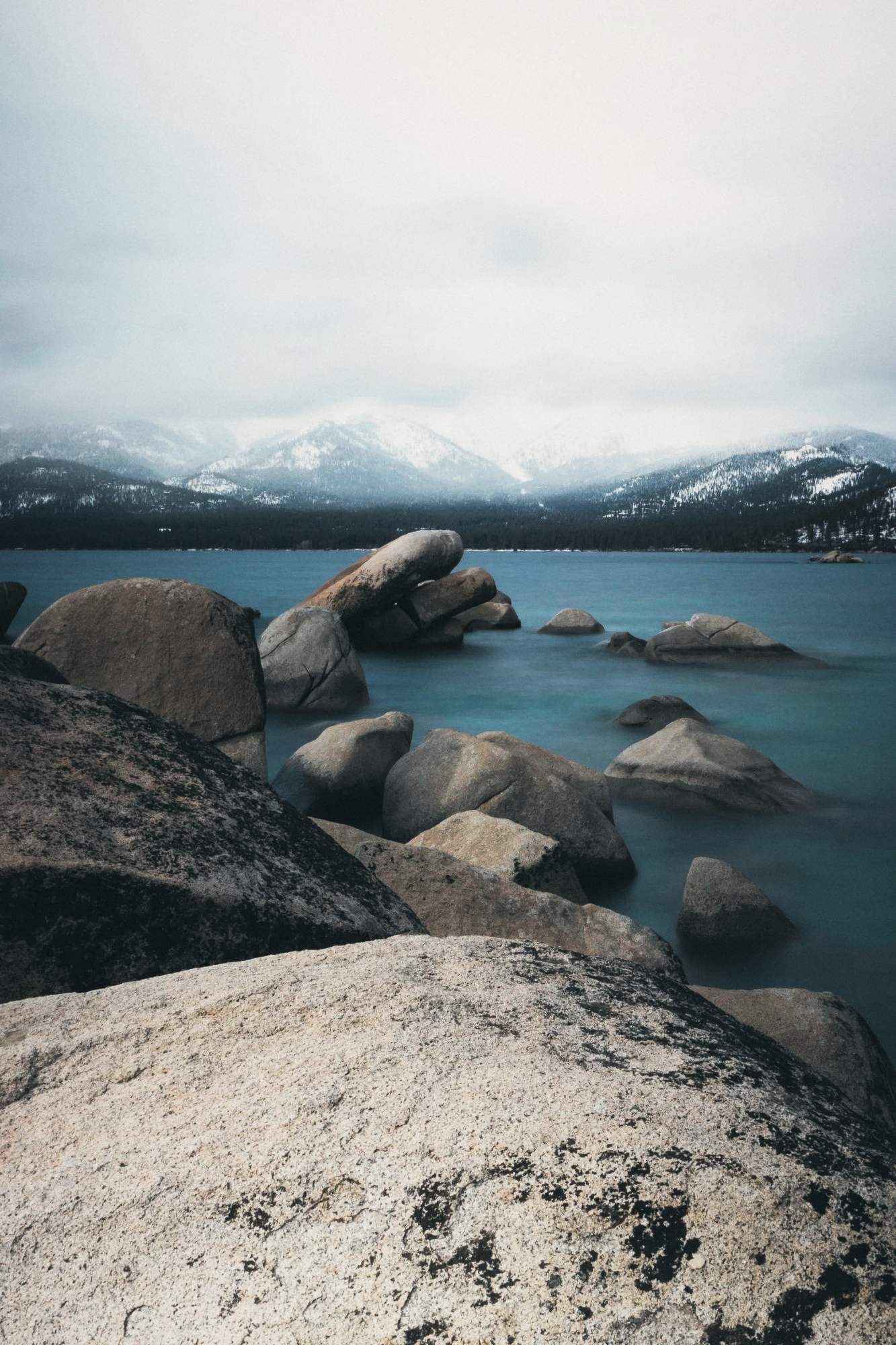 A Lake Tahoe shoreline under snow, granite boulders in clear water.