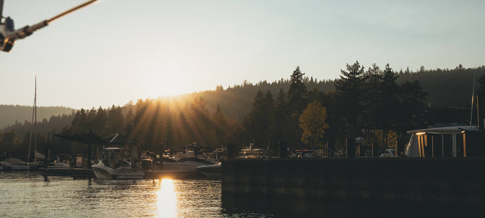 The sun dropping behind the pines at a Lake Tahoe marina, its reflection on the water by the docks.
