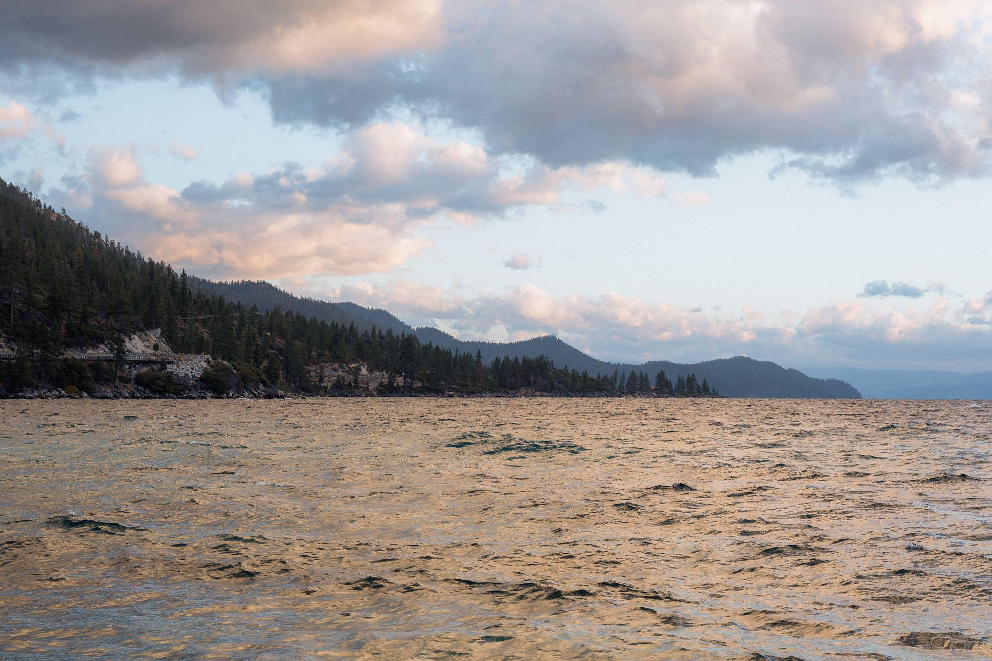 Lake Tahoe's East Shore from the water: forested slopes, granite and the highway along the shore under evening cloud.