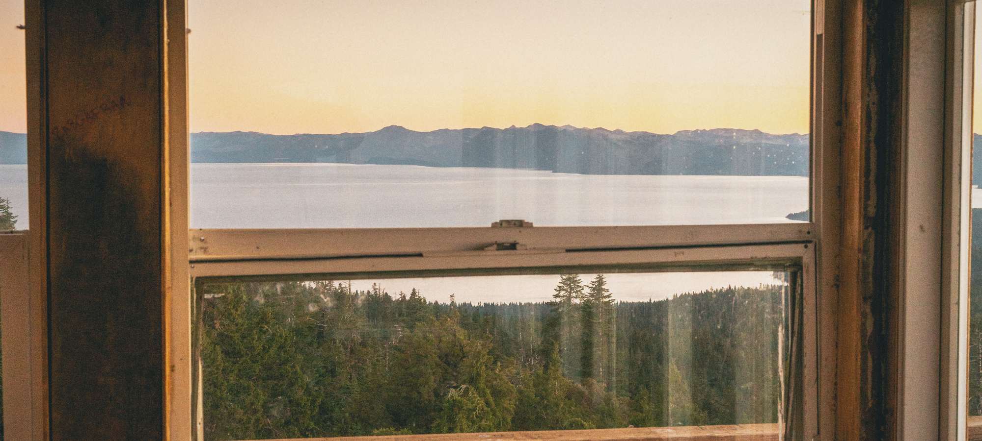 Lake Tahoe at sunset through a window of the Martis Peak fire lookout, forest below the sill.